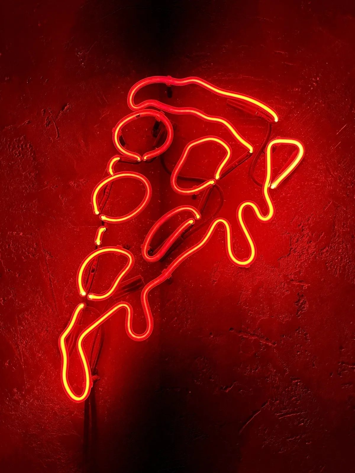 Ein rotes Neonlicht in Form eines Pizzastücks leuchtet vor einem dunklen Hintergrund.