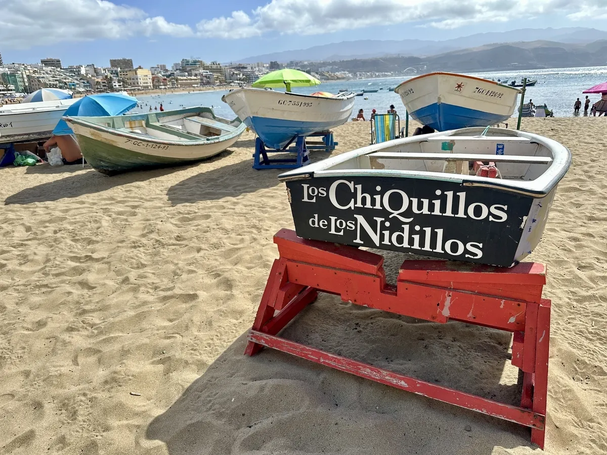 Boote stehen am Sandstrand mit Blick auf das Meer und die Stadt im Hintergrund.