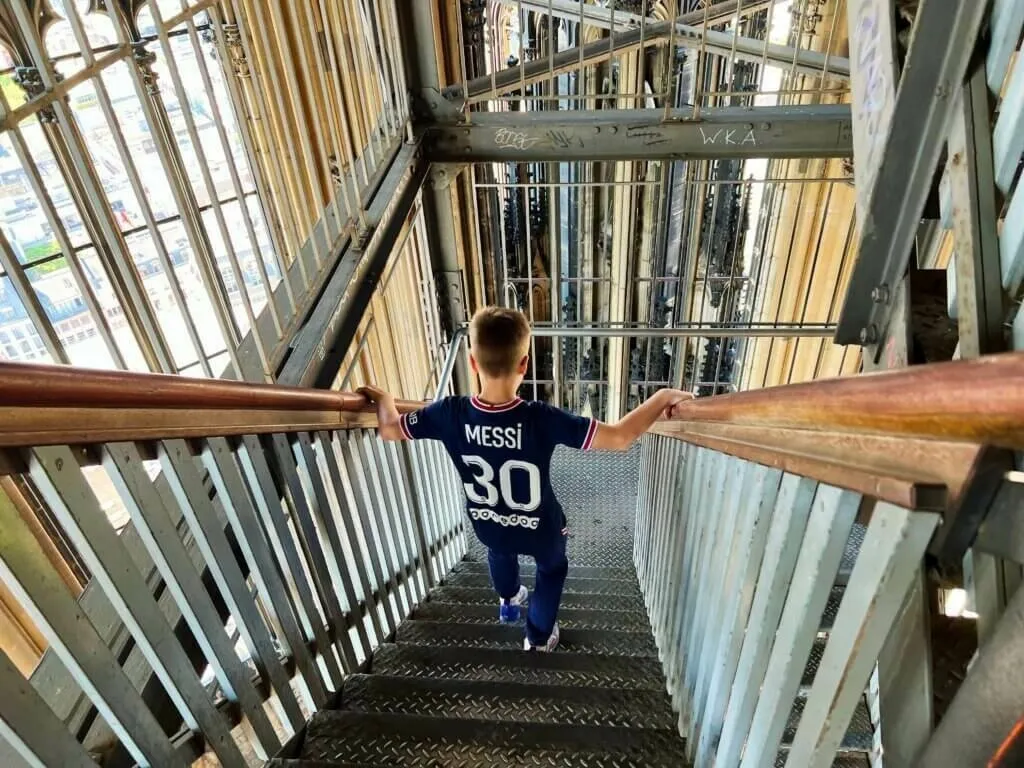 Ein Junge im Fußballtrikot (mit der Nummer 30) steigt die Metalltreppe im Turm des Kölner Doms hinab.