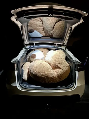 Der Kofferraum eines Tesla Model Y ist geöffnet und einen sehr großen Plüschbärchen, der dicht zusammengedrängt ist. Der Innenraum ist schwach beleuchtet, was den Bären hervorhebt.