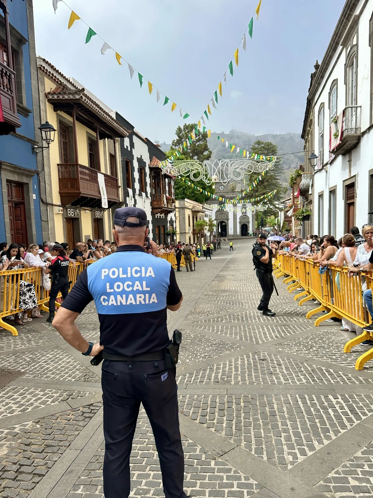 Ein Polizeibeamter der Policía Local sichert eine von Zuschauern gesäumte Straße während einer Veranstaltung in einer Stadt.