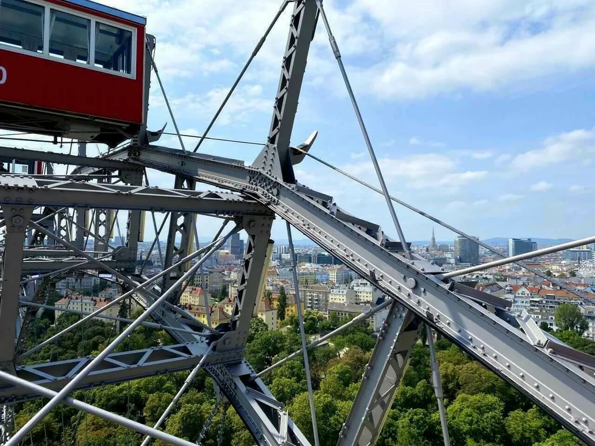 Blick aus einer roten Gondel des Wiener Riesenrads über die massive Stahlkonstruktion und die dahinterliegende Skyline von Wien.