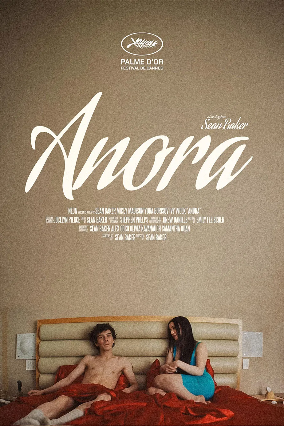 Ein Mann und eine Frau sitzen auf einem Bett in einem Schlafzimmer. Der Raum ist minimalistisch eingerichtet, mit klaren Wänden und einem neutralen Farbschema. Im oberen Bereich des Bildes steht der Titel des Films „Anora“ sowie die Auszeichnung „Palme d'Or“.