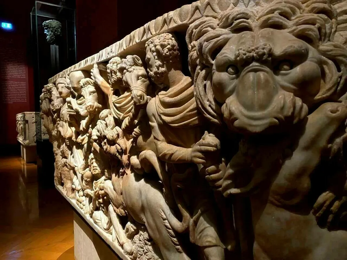 Ein detailliertes, reliefartiges Fragment eines antiken römischen Sarkophags aus Stein, das eine Szene mit Figuren und einem Löwenkopf zeigt, im kunsthistorisches Museum Wien.