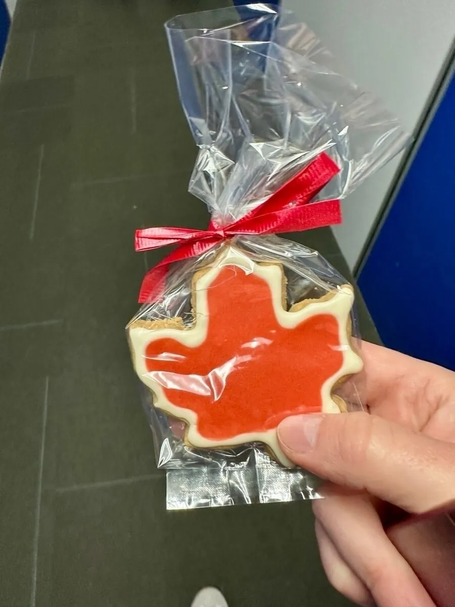 Eine Person hält einen in Plastik verpackten Keks in Form eines Ahornblatts mit roter Glasur.