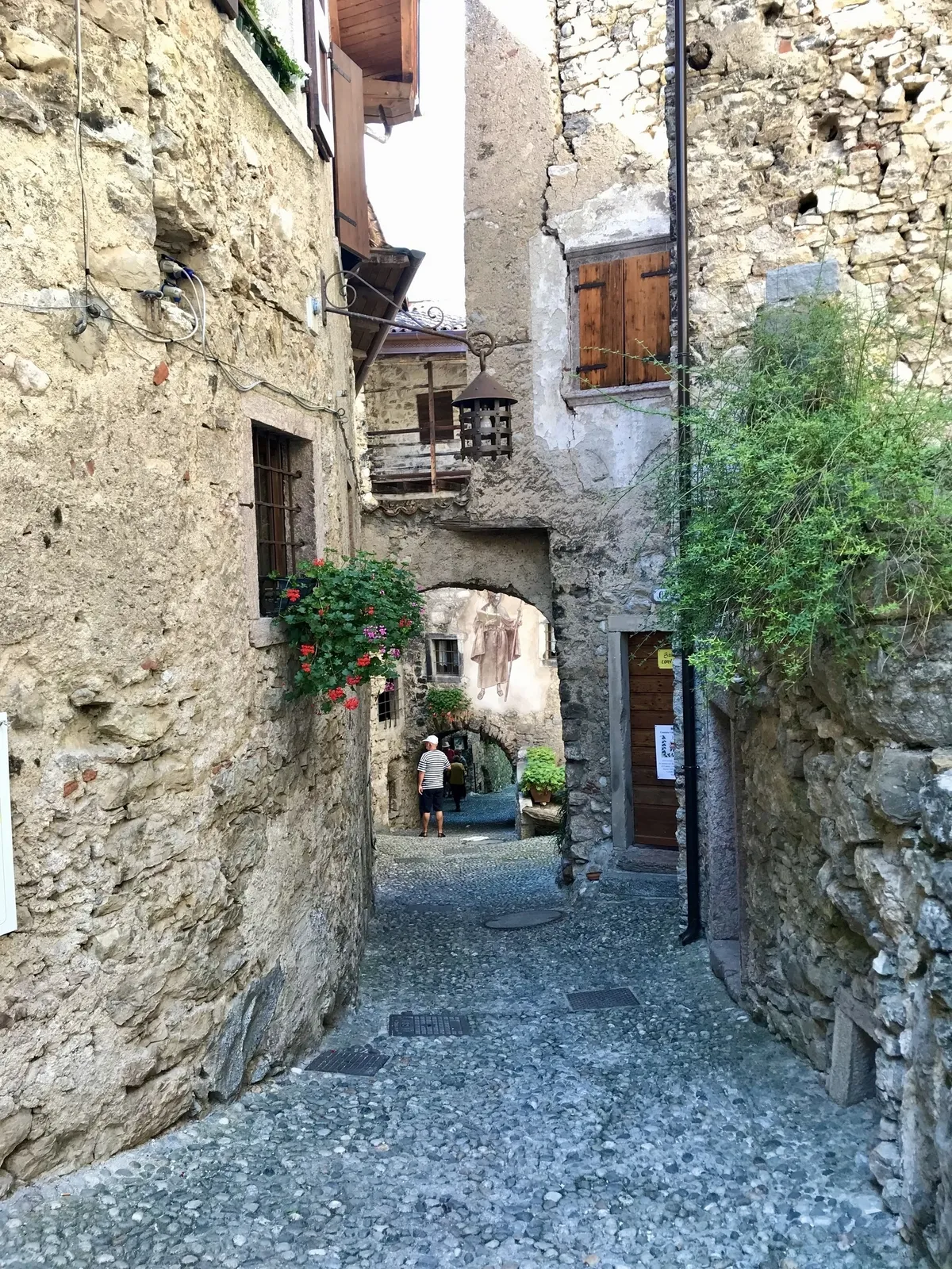 Eine enge, malerische Gasse in dem historischen Dorf Canale di Tenno mit alten Steinwänden, Pflanzen und einem kleinen bogenförmigen Durchgang.
