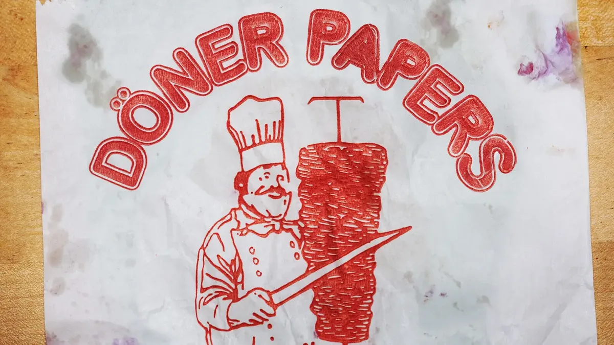 Das ikonische Döner-Logo: Ein Koch schneidet Fleisch von einem vertikalen Spieß, umgeben vom Text DÖNER PAPERS.
