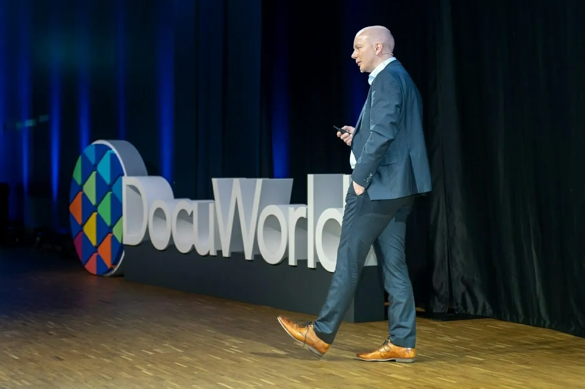René Fischer läuft über eine Holzbühne vor dem großen „DocuWorld“-Schriftzug.