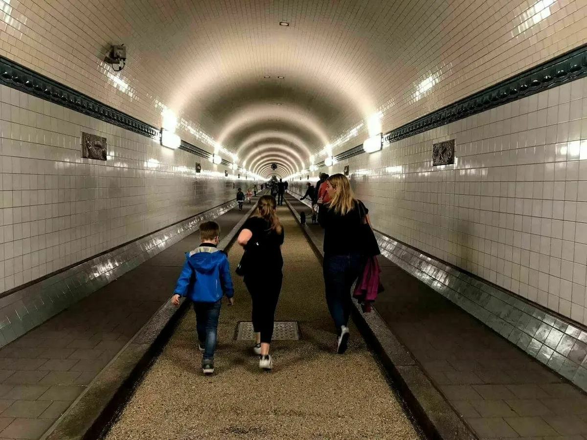 Eine Familie geht durch den weiß gekachelten Wände Alten Elbtunnel in Hamburg.
