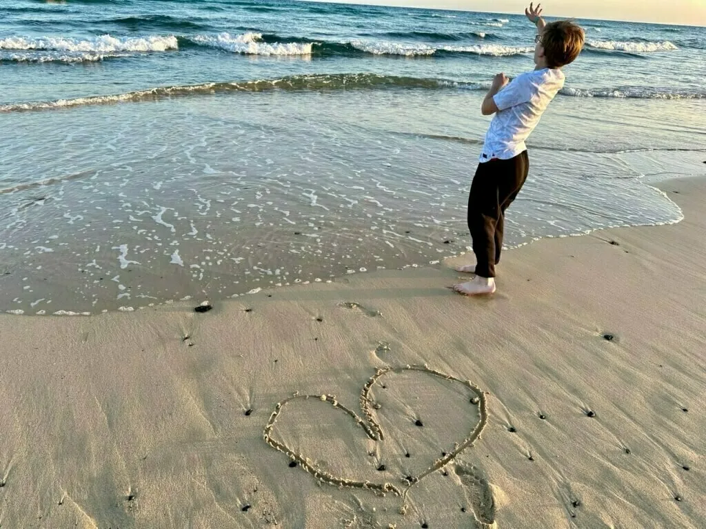 Der Sohnemann hat ein Herz in den Sand am Strand von Fuerteventura gemalt und wirft Steine in die Wellen.