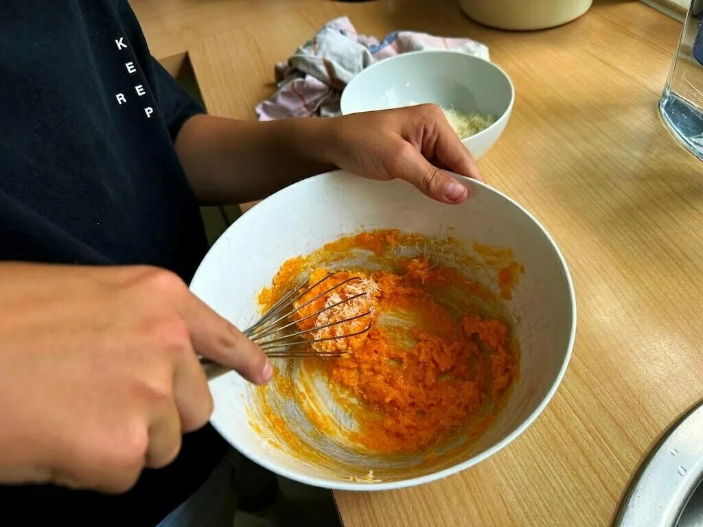 Eine Person rührt einen Teig mit einer orangenen Masse in einer Schüssel.