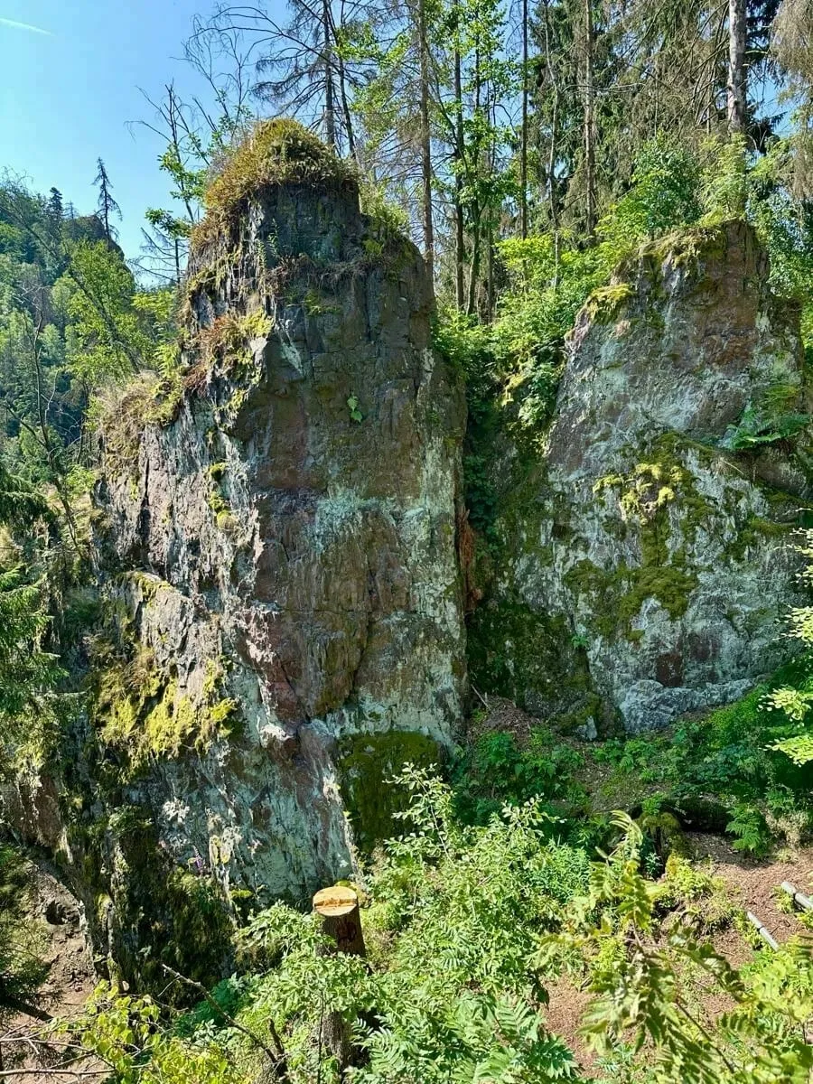 Der sogenannte Hufeisenstein bei Bad Tabarz. Ein felsiger, bewaldeter Hang mit üppiger Vegetation und vereinzelten Bäumen erstreckt sich unter strahlend blauem Himmel.