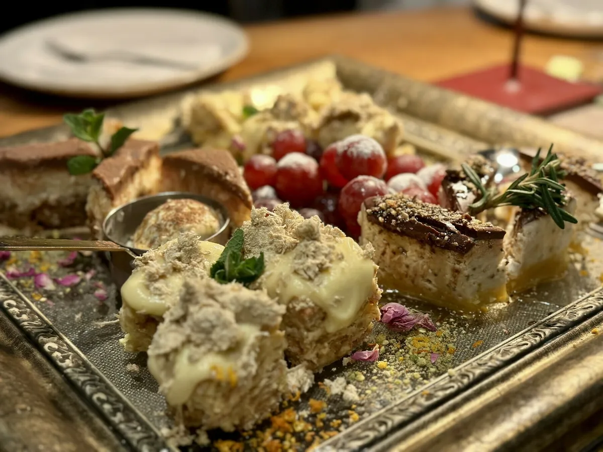 Ein Dessert-Sampler auf einem rechteckigen, verzierten Tablett mit verschiedenen Kuchenstücken, belegt mit Puder, Minze und umgeben von frischen roten Beeren.