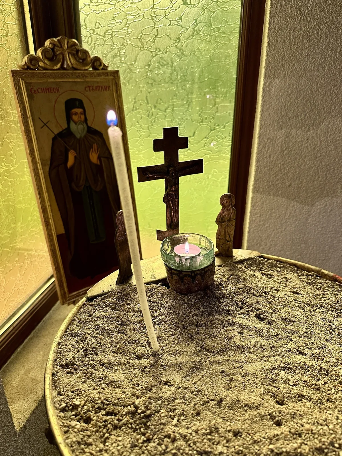 Ein Altar mit einer Ikone, zwei Kerzen, einem Kreuz in einem sandgefüllten Becken in der Tsarska Bistritsa in Borovets, Bulgarien.