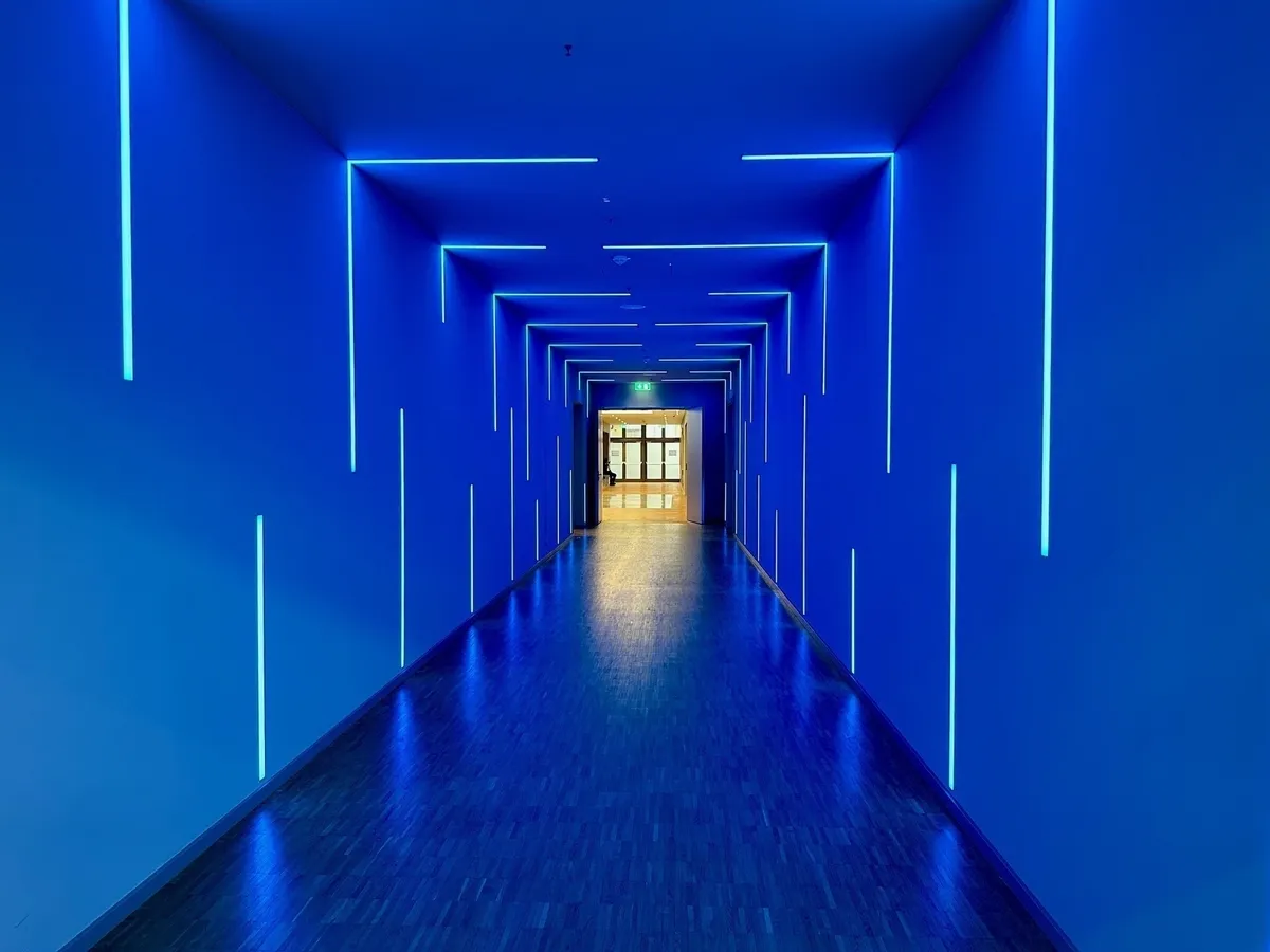 Ein langer, symmetrischer Korridor, beleuchtet in leuchtendem Blau mit vertikalen und horizontalen Neonstreifen.