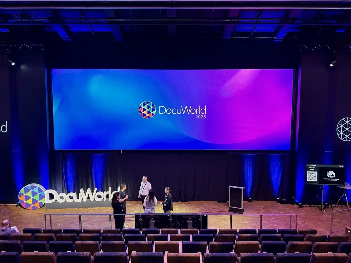 Weitwinkelaufnahme einer großen Bühne mit der Leinwand „DocuWorld 2025“ und leeren Sitzreihen im Auditorium.