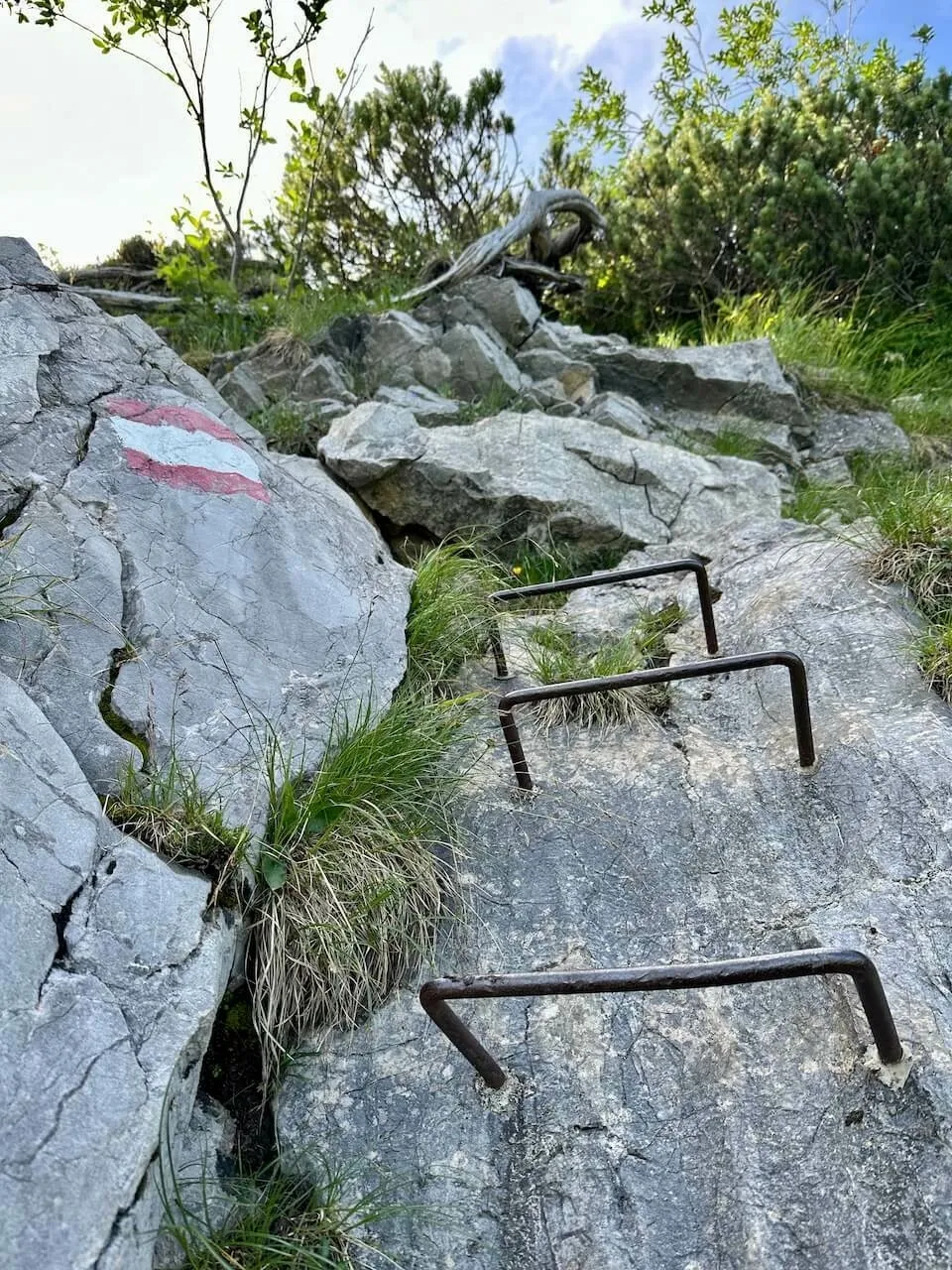 Felsiger Klettersteig-Abschnitt mit fest verankerten Eisenbügeln als Steighilfen und rot-weiß-roter Markierung auf dem Felsen