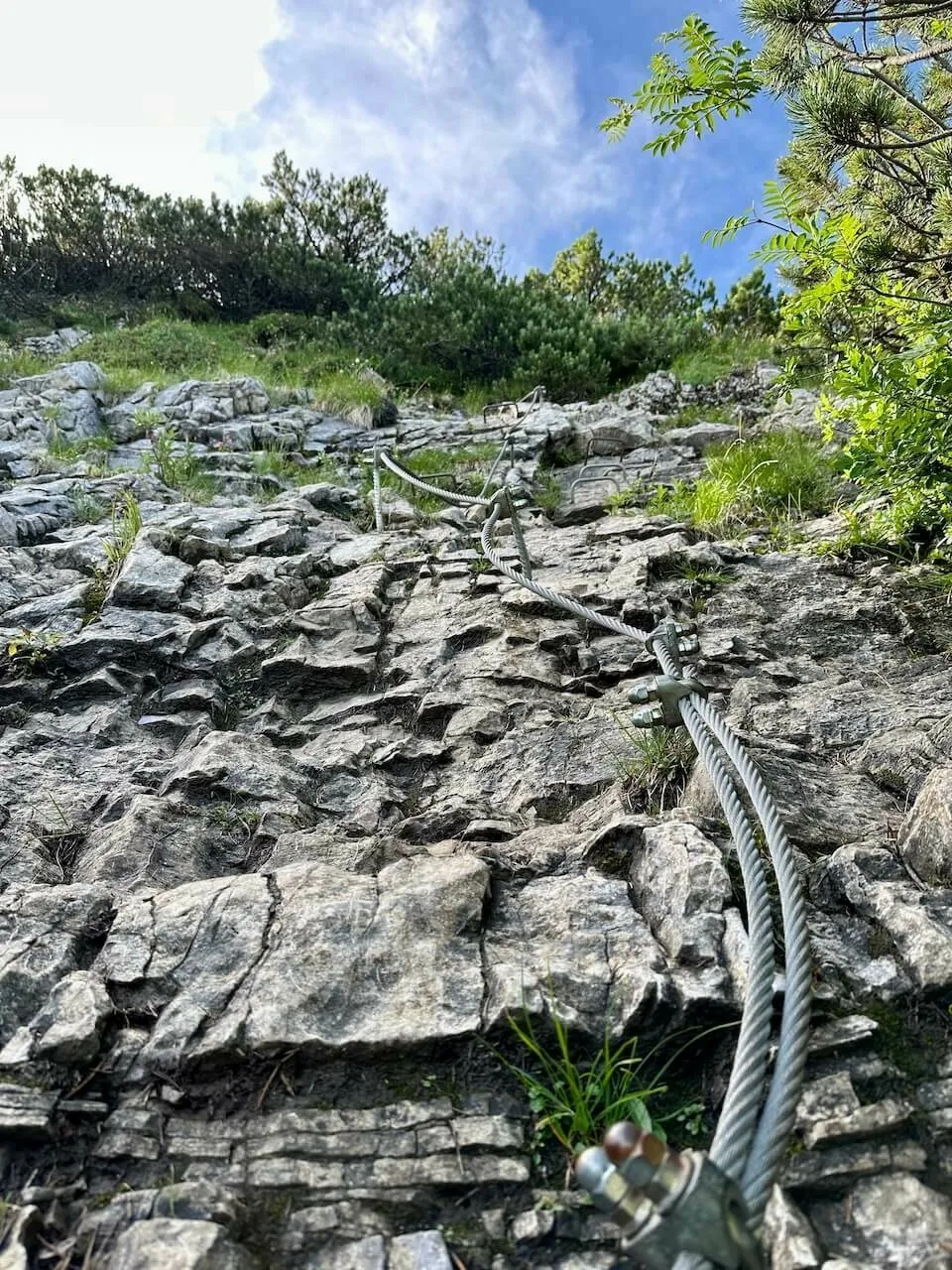 Aufnahme von unten auf eine steile Felswand, durch die ein dickes Sicherungs-Stahlseil (Klettersteig) verläuft