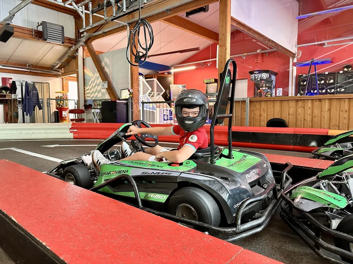 Eine Person in roter Kleidung und Helm sitzt in einem grünen Gokart in einer Halle.
