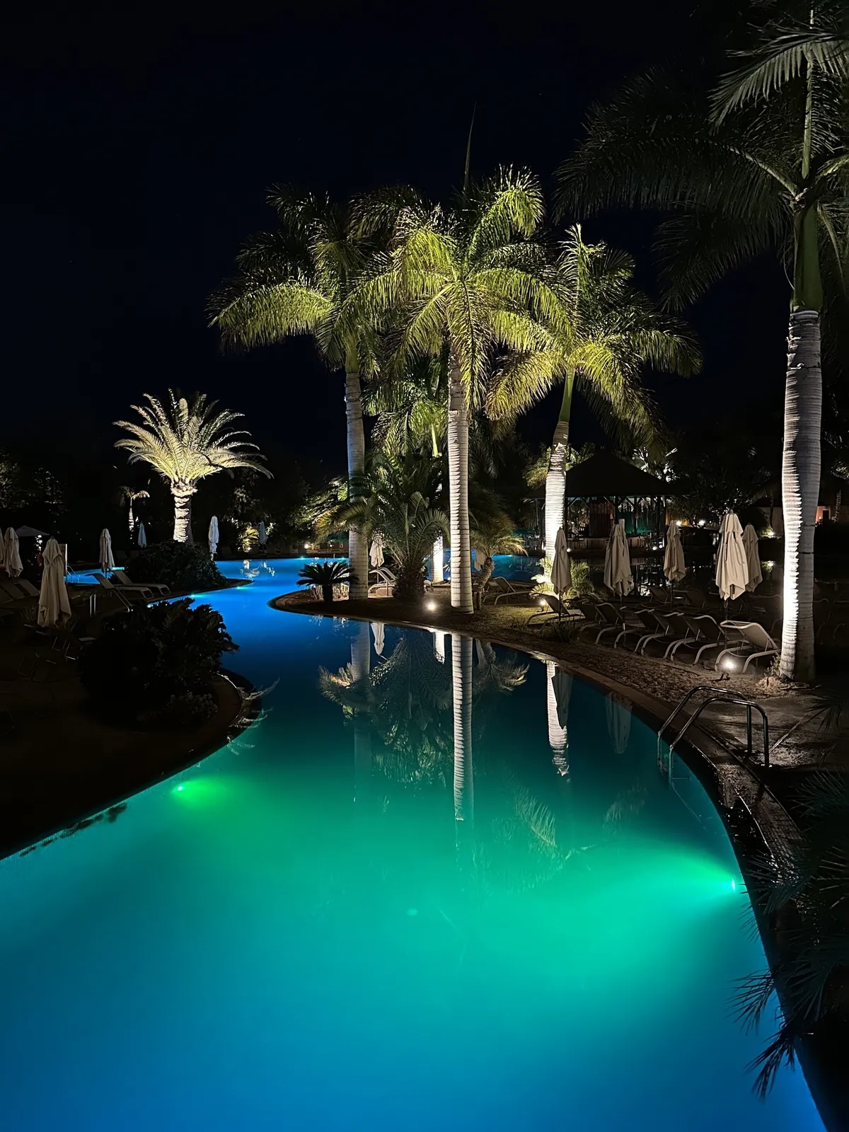 Ein beleuchteter Pool mit umgebenden Palmen schafft eine entspannte Atmosphäre in der Nacht.