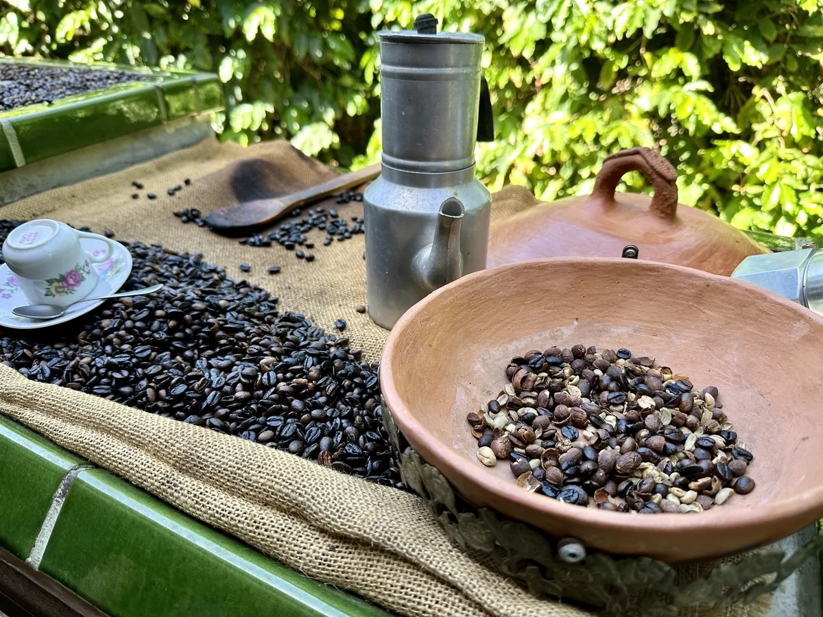 Eine Szene zeigt frische und geröstete Kaffeebohnen in Schüsseln neben einer Espressokanne und einer Tasse auf einem mit Jute gedeckten Tisch im Freien.
