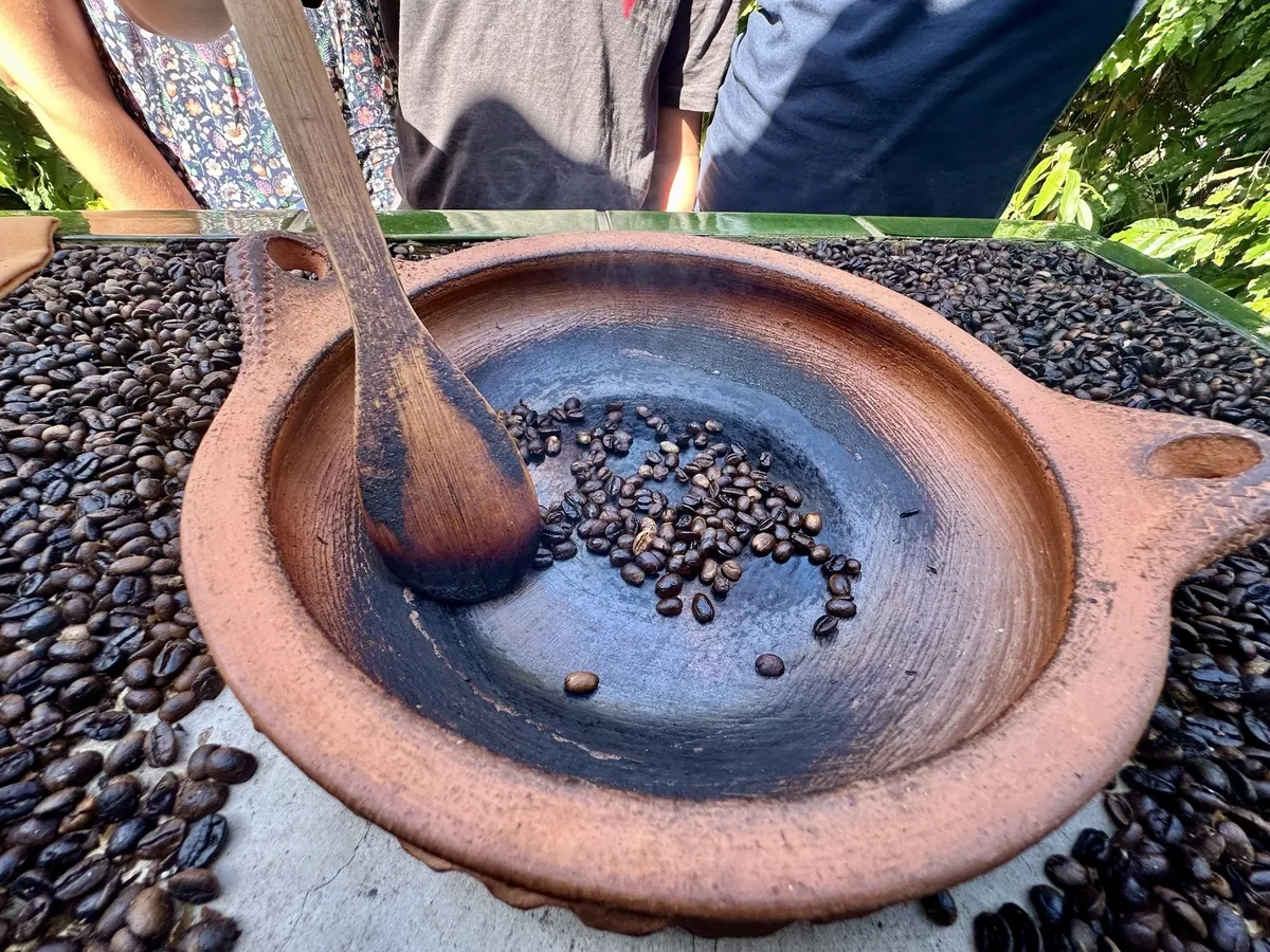 Ein Holzlöffel rührt in einem traditionellen Tonbehälter, der von Kaffeebohnen umgeben ist.