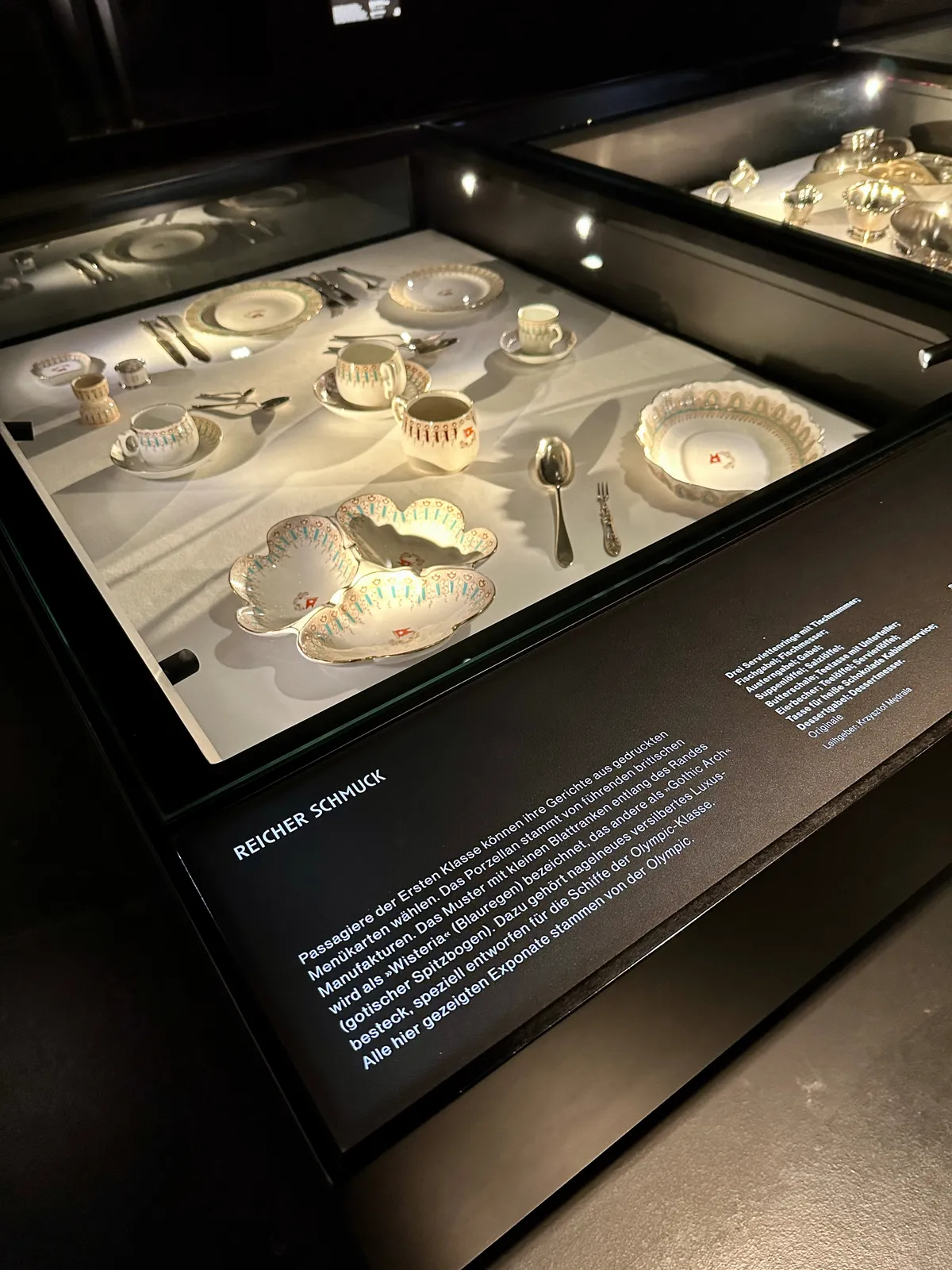 Ein Set aus elegantem Geschirr und Besteck der ersten Klasse der Titanic wird in einer beleuchteten Vitrine präsentiert.