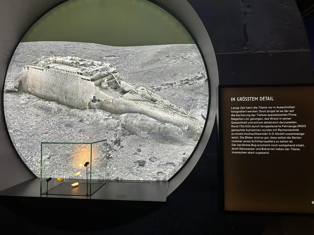 Ein großer Bildschirm zeigt das Wrack der Titanic auf dem Meeresgrund, begleitet von einer Infotafel mit Hintergrundinformationen.