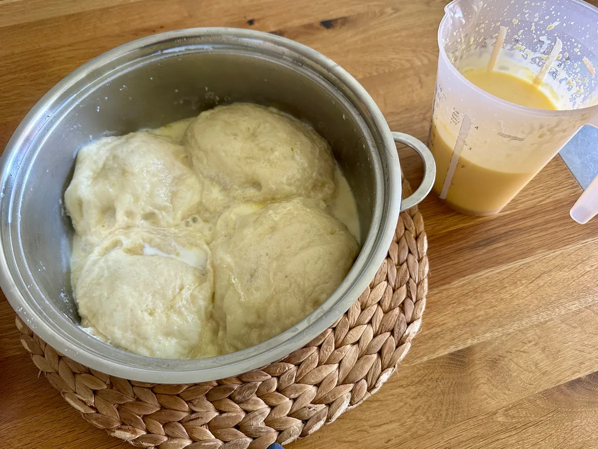 Ein Topf mit Dampfnudeln oder auch Hefeklösen neben einem Becher mit einer Vanillesauce auf einem Tisch.