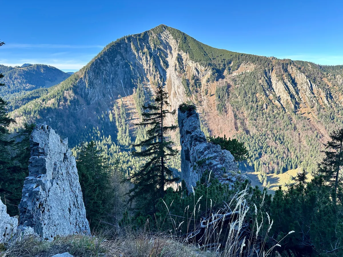 Blick auf die Brecherspitz mit bewaldeten Hängen und markanten Felsformationen erstrecken sich unter einem klaren blauen Himmel.