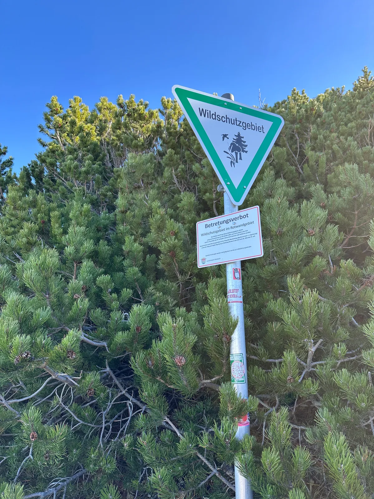 Ein Schild des Wildschutzgebiets am Jägerkamp vor einem Hintergrund mit grünen Bäumen und blauem Himmel.