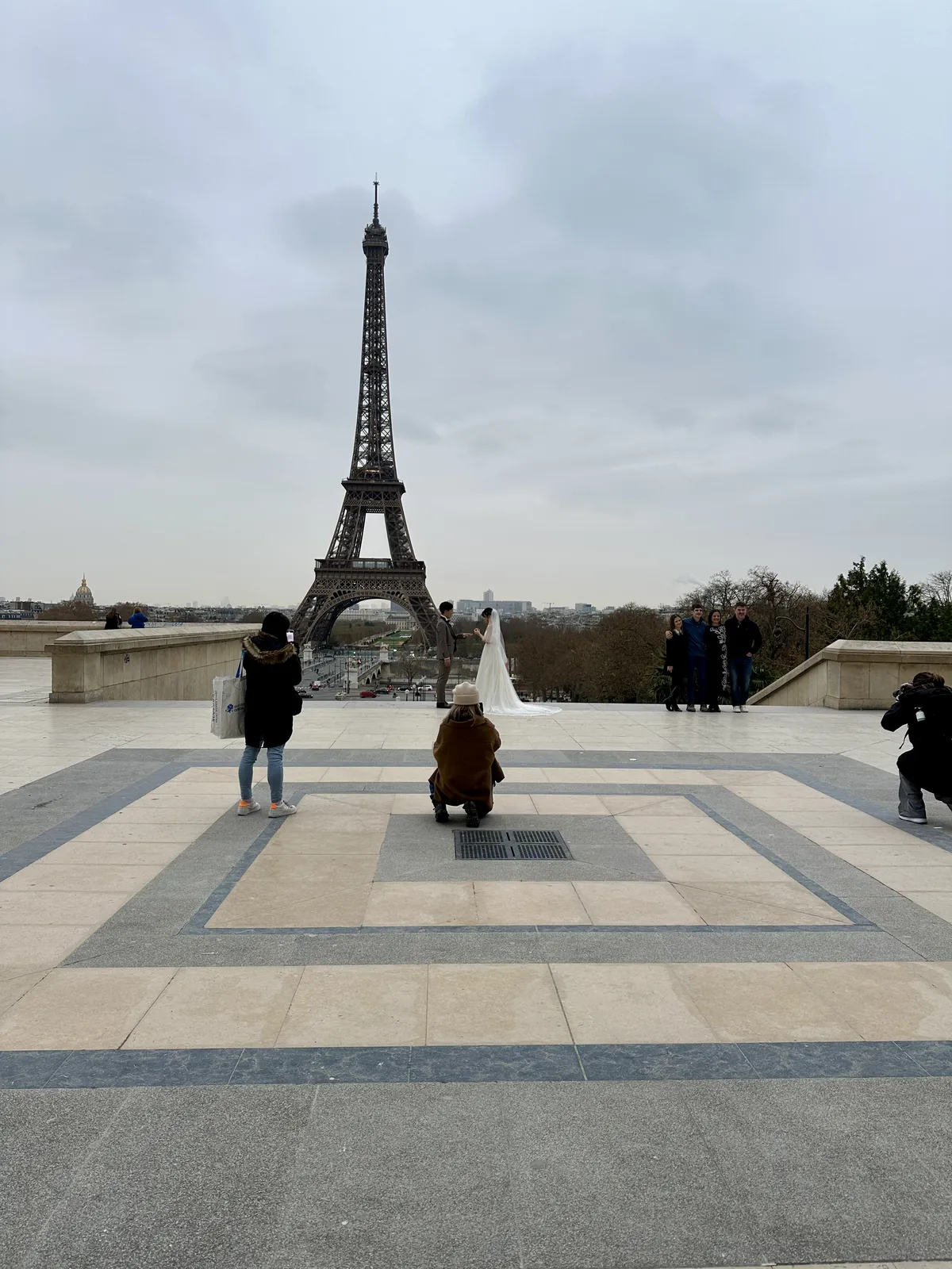 Ein Hochzeitspaar posiert vor dem Eiffelturm in Paris, während ein Fotograf und mehrere Personen sie fotografieren.