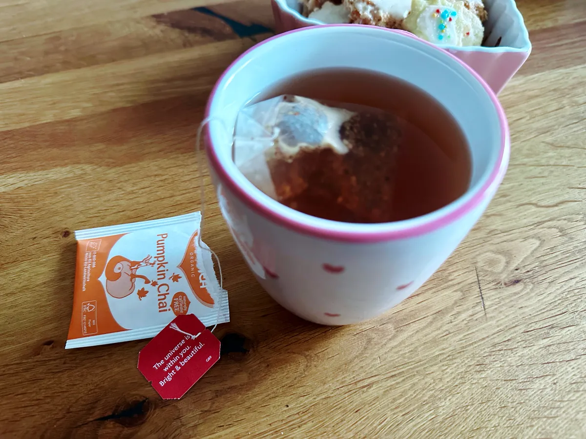 Tasse Pumpkin-Chai-Tee auf einem Holztisch, daneben die geöffnete Teeverpackung und ein Etikett mit dem Spruch "The universe is within you. Bright & beautiful.".