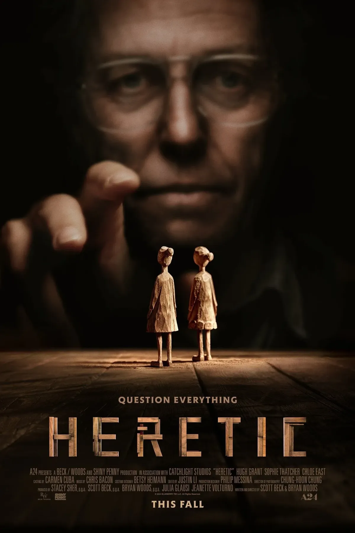 Ein Horrorfilm-Poster zeigt eine zerstörte Szenerie mit düsterer Beleuchtung. Ein übergroßes Gesicht überragt zwei kleine Holzfiguren, die eng nebeneinander stehen, während eine Hand drohend auf sie zeigt. Der Text 