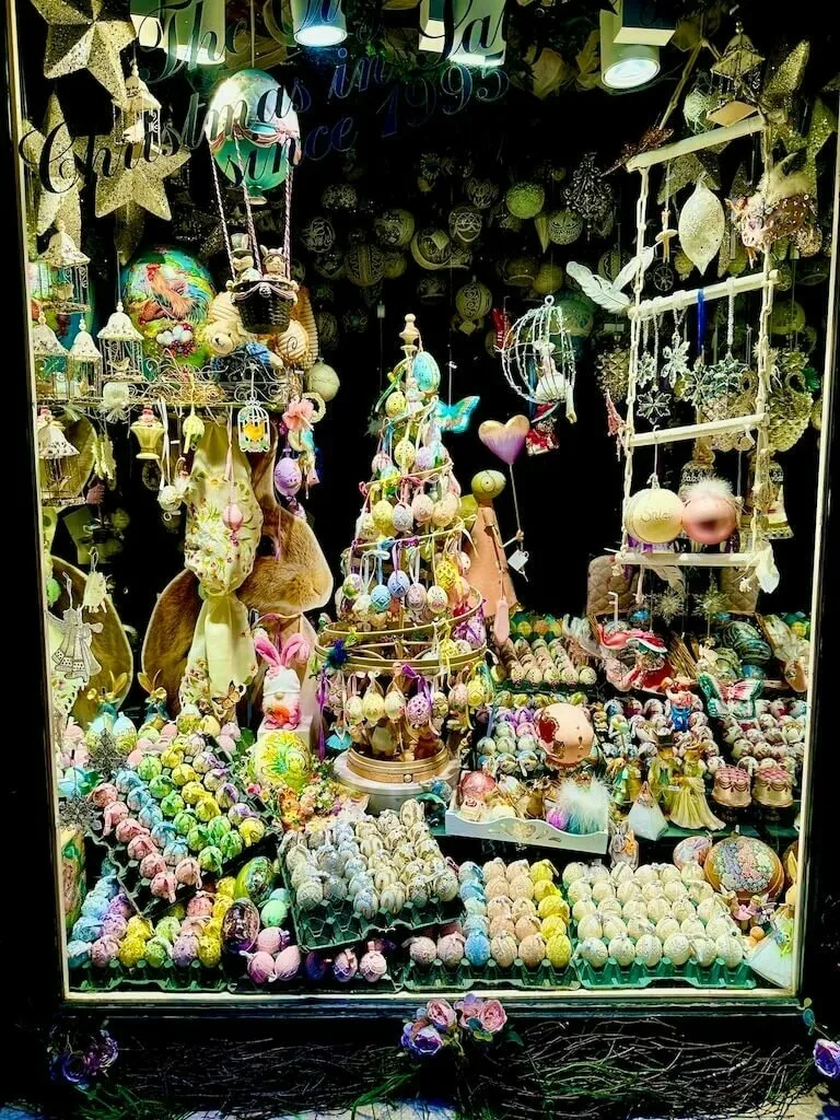 Ein festlich dekoriertes Schaufenster zeigt bunte Ostereier, zahlreiche Dekorationen und ein zentrales Baumornament.