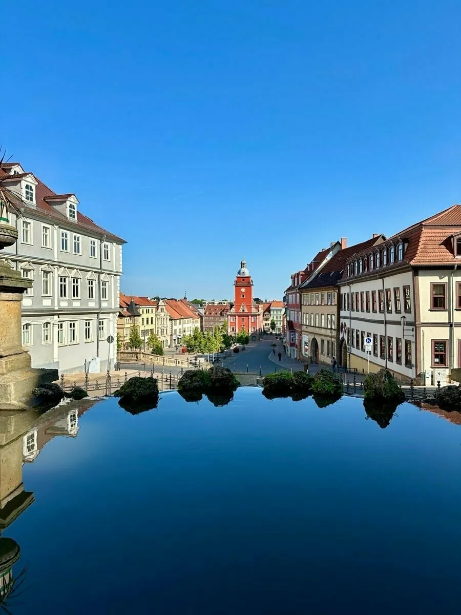 Die Wasserkunst mit Blick auf die historische Innenstadt von Gotha, und einem zentralen Brunnen spiegelt sich im ruhigen Wasser wider.