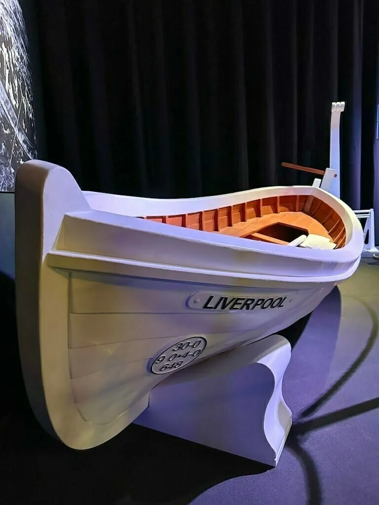 Ein Nachbau eines weißen Rettungsbootes, beschriftet mit "LIVERPOOL" an der Seite, ausgestellt in einem abgedunkelten Ausstellungsraum.