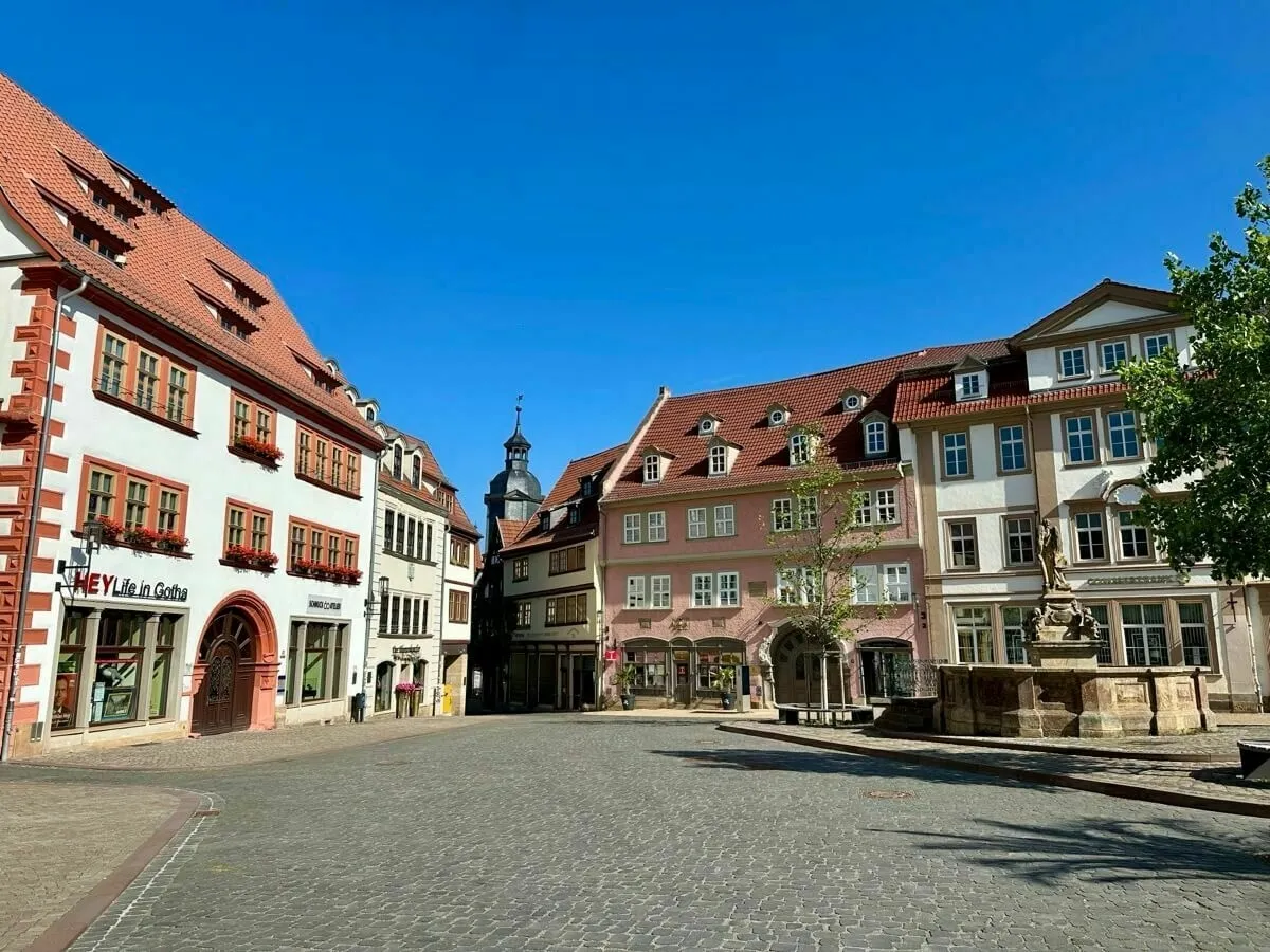 Der malerische Marktplatz von Gotha mit alten, charmanten Gebäuden und einem Brunnen unter strahlend blauem Himmel.