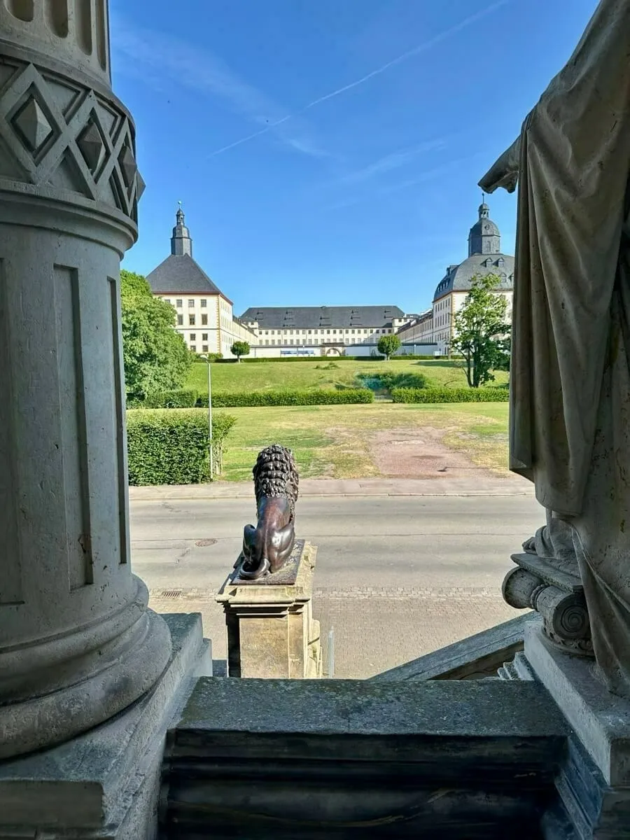 Die Aussicht vom herzoglichen Museum auf das Schloss Friedenstein, einem Löwenstatuen-Denkmal im Vordergrund und gepflegten Rasenflächen.