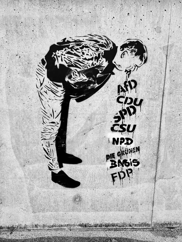 Ein Graffiti zeigt eine Person, die sich übergibt, wobei die Namen verschiedener deutscher politischer Parteien aus ihrem Mund kommen.