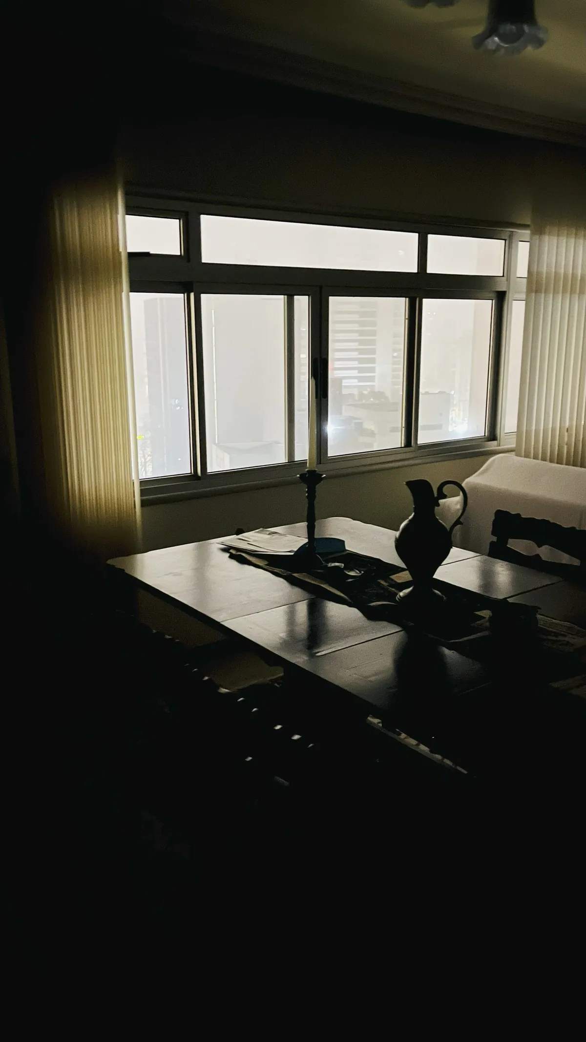 photo of a semi-dark living room, outside the big window, the city scape can barely be seen with all the mist.