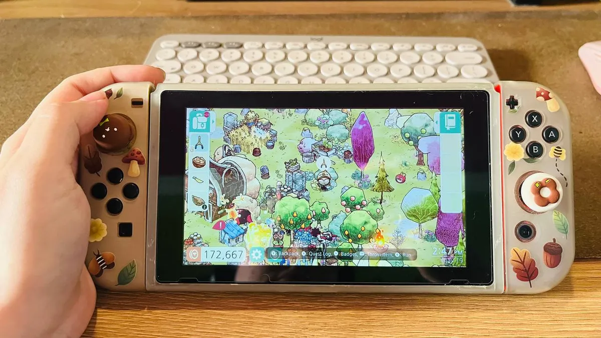 Picture of my Nintendo Switch with cute brown bear thumb grips and protective case with an autumn/leafy theme; on the screen, the game Cozy Grove.