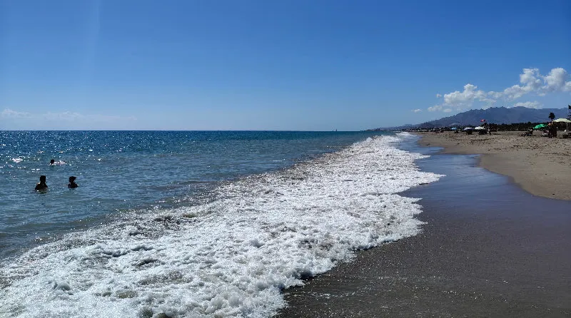 Photo of the sea, the beach, and blue sky, with people in the water
