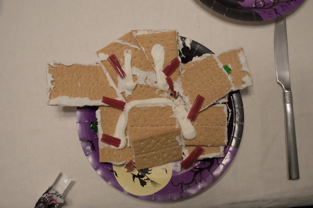 A pile of graham crackers covered in white icing and licorice is strewn about. A frowny face is drawn over the rubble. Gummy bears lay underneath.