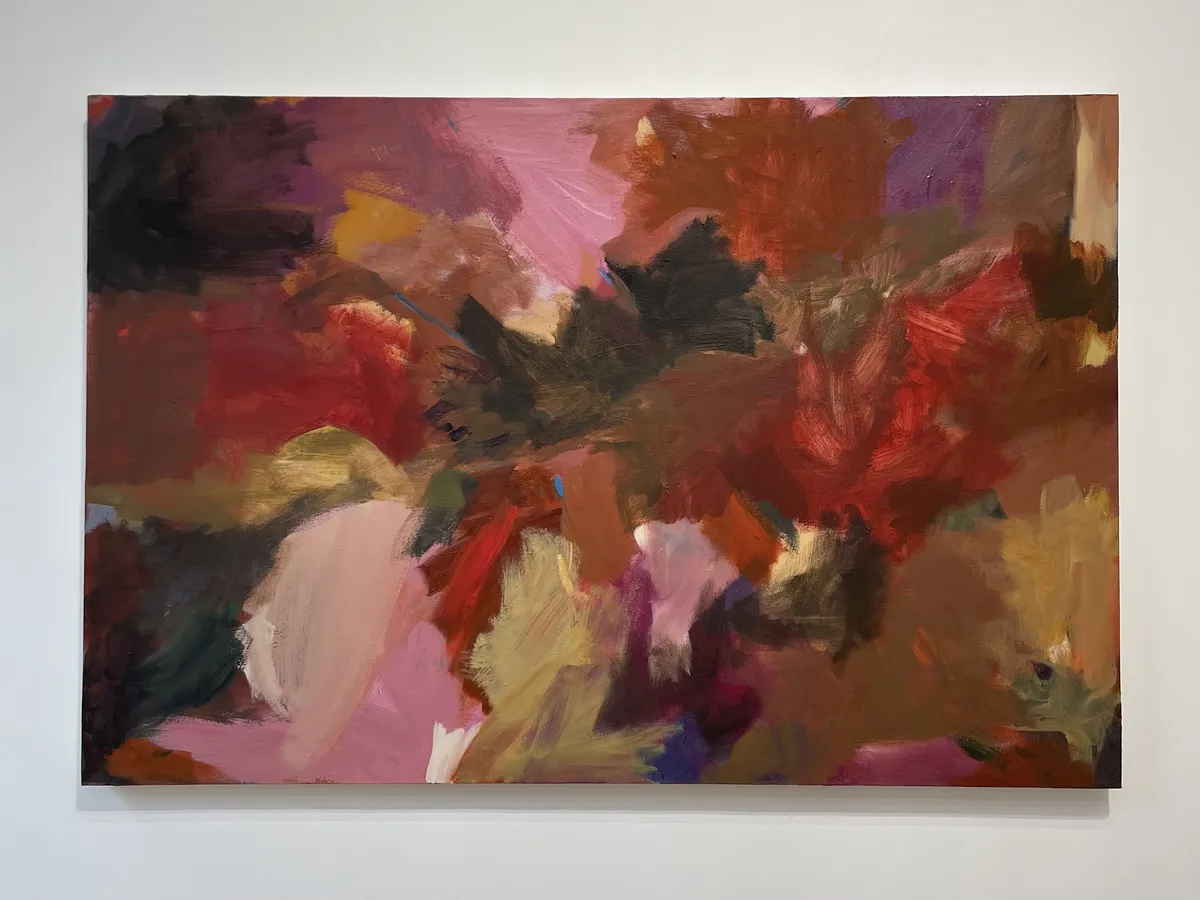 A large abstract painting with areas of pinks, reds, and browns, on a white wall