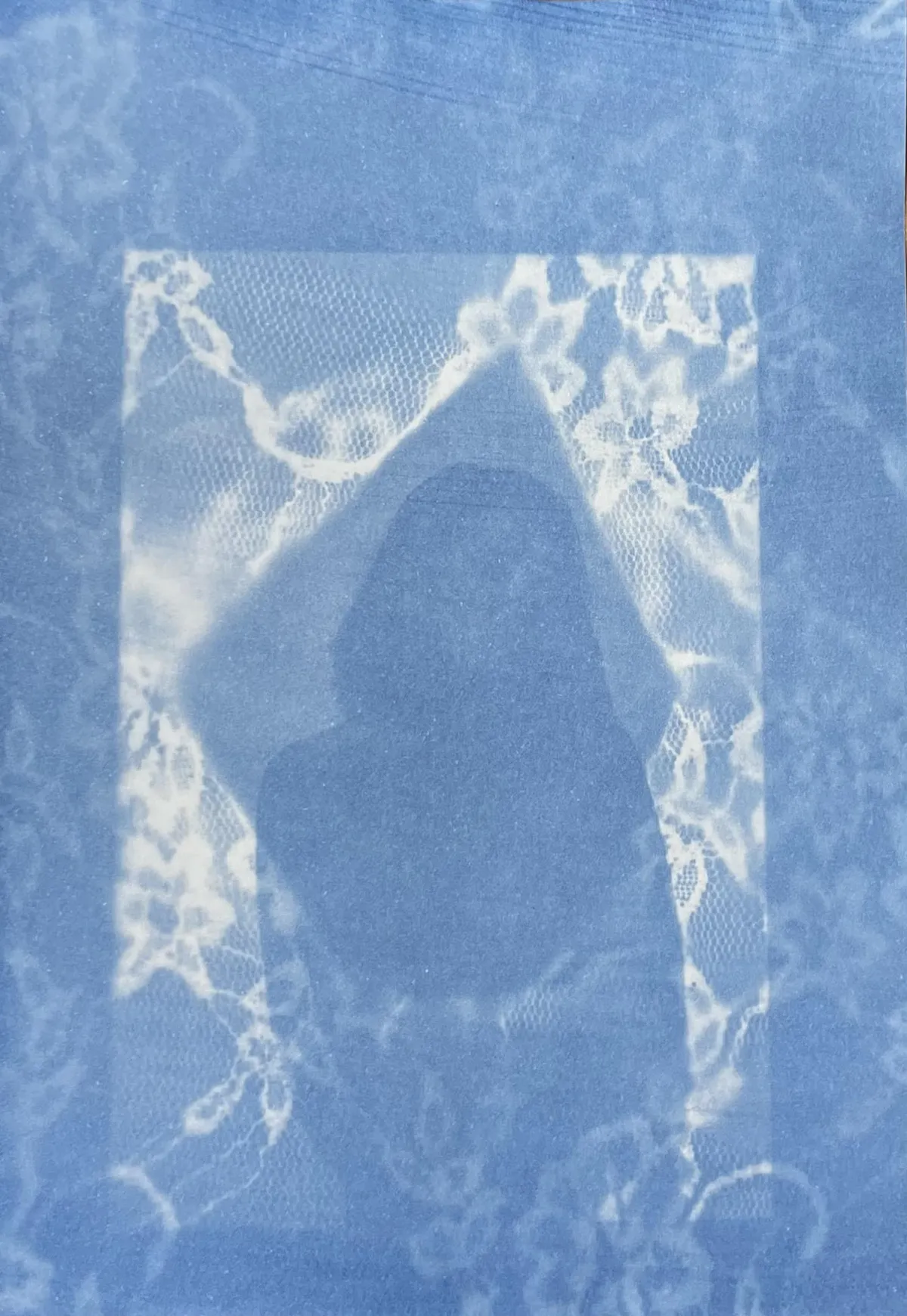 A cyanotype image of lace fabric cut back to reveal a shadowy figure looking at the viewer
