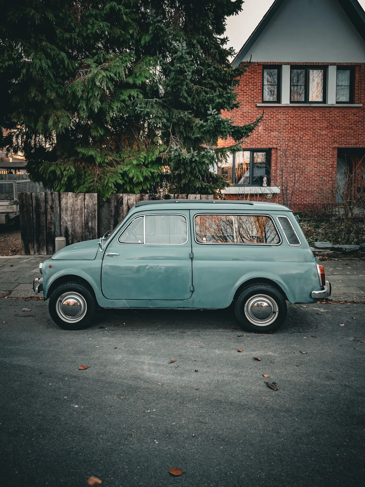 A car parked in the street in front of a house and tree