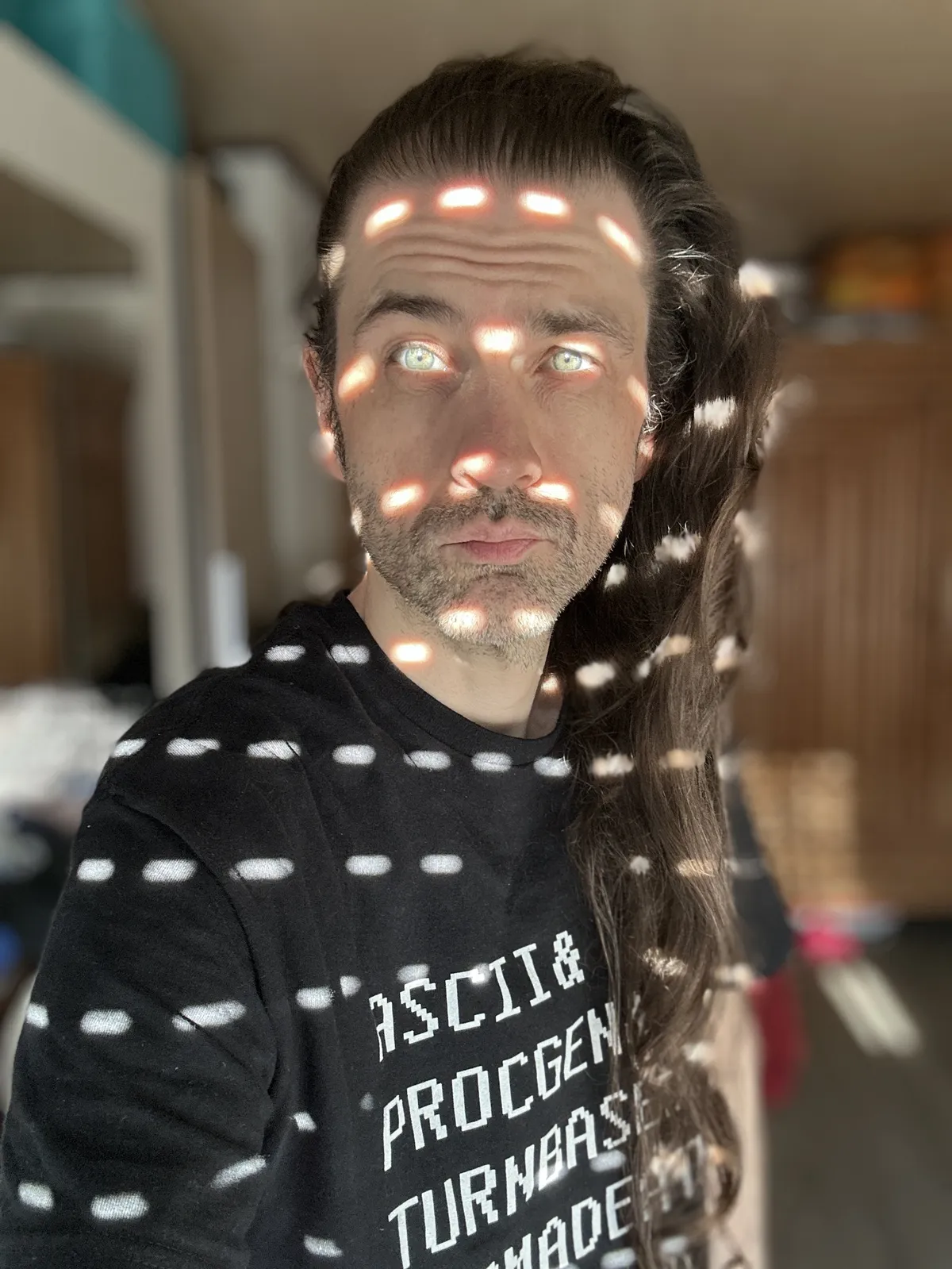 Some middle aged white dude with hair that has been growing for 1986 days, indoors, with a blurry background and light dots all over. Two of the light dots light up the eyes.