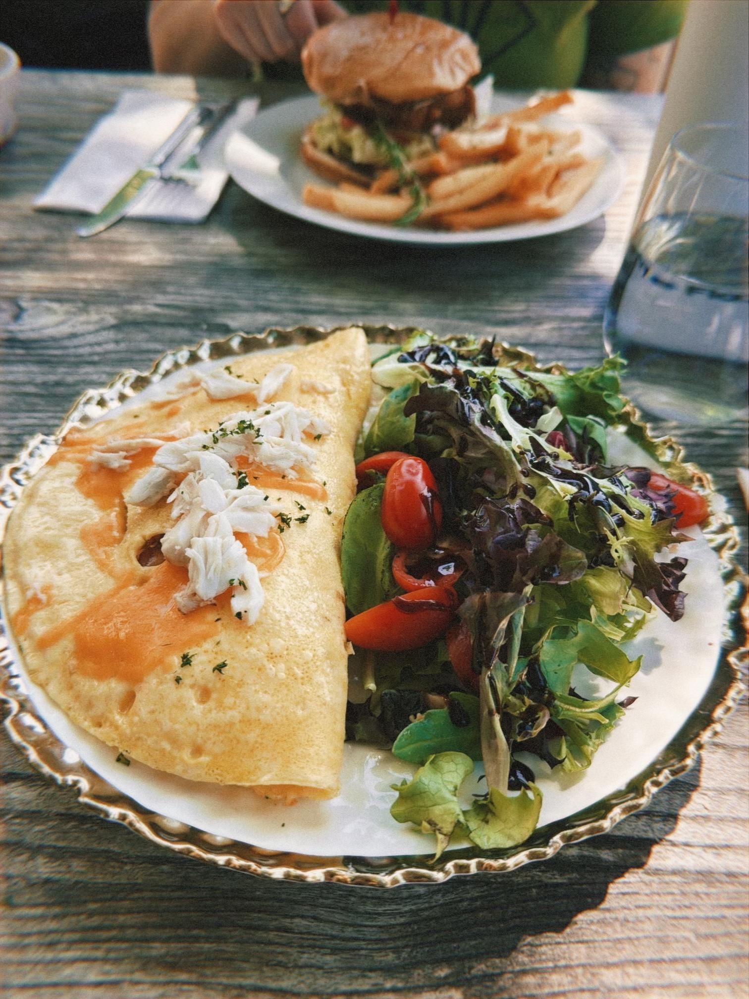 A plate of omelette with a side salad. A burger in the background