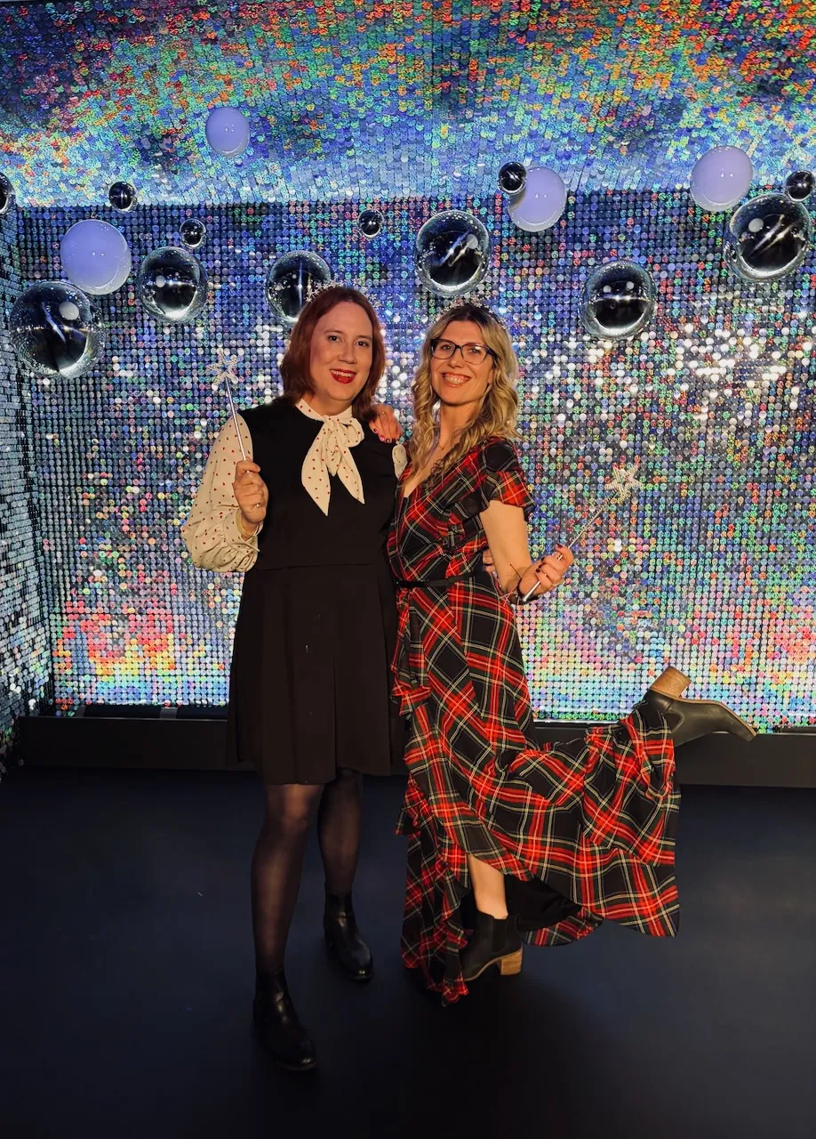 Two women posing in front of a sparkle backdrop